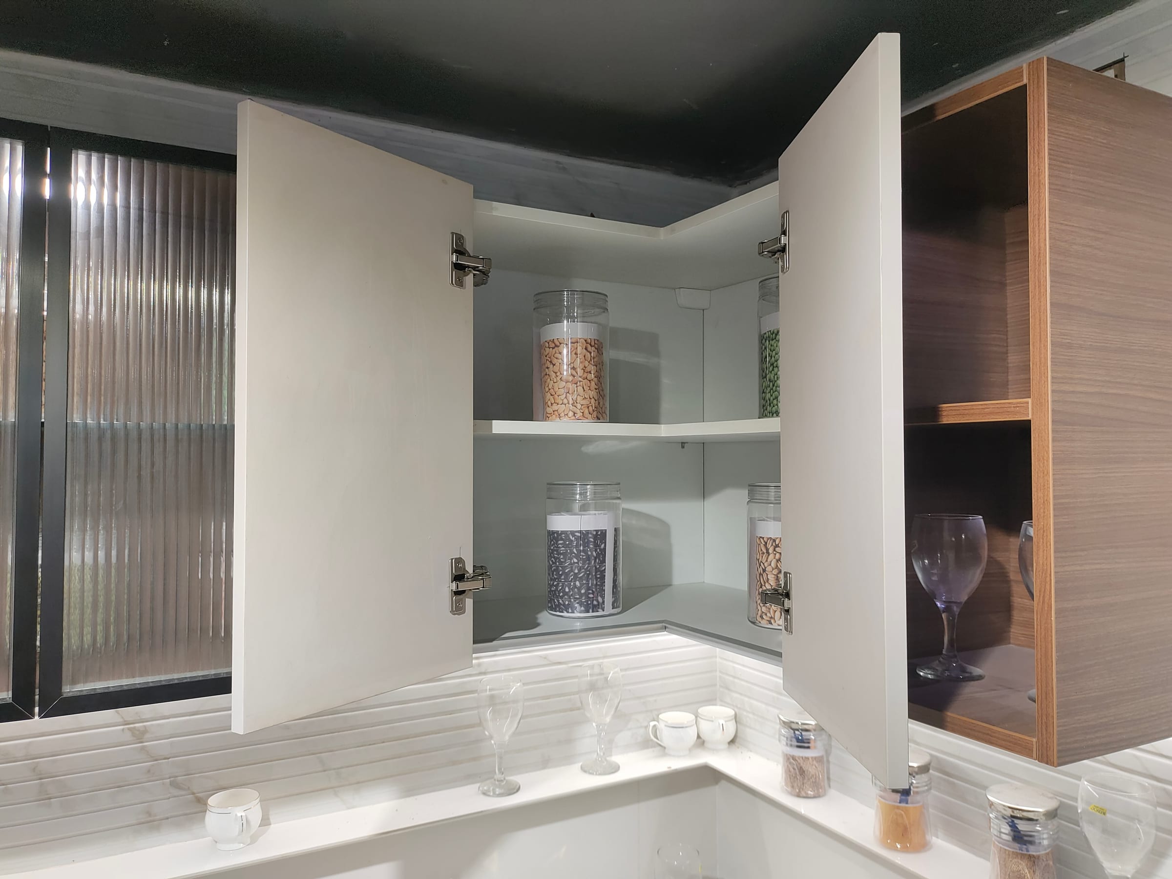A corner wall cabinet with both doors open, showing a continuous L-shaped shelf running around the internal corner