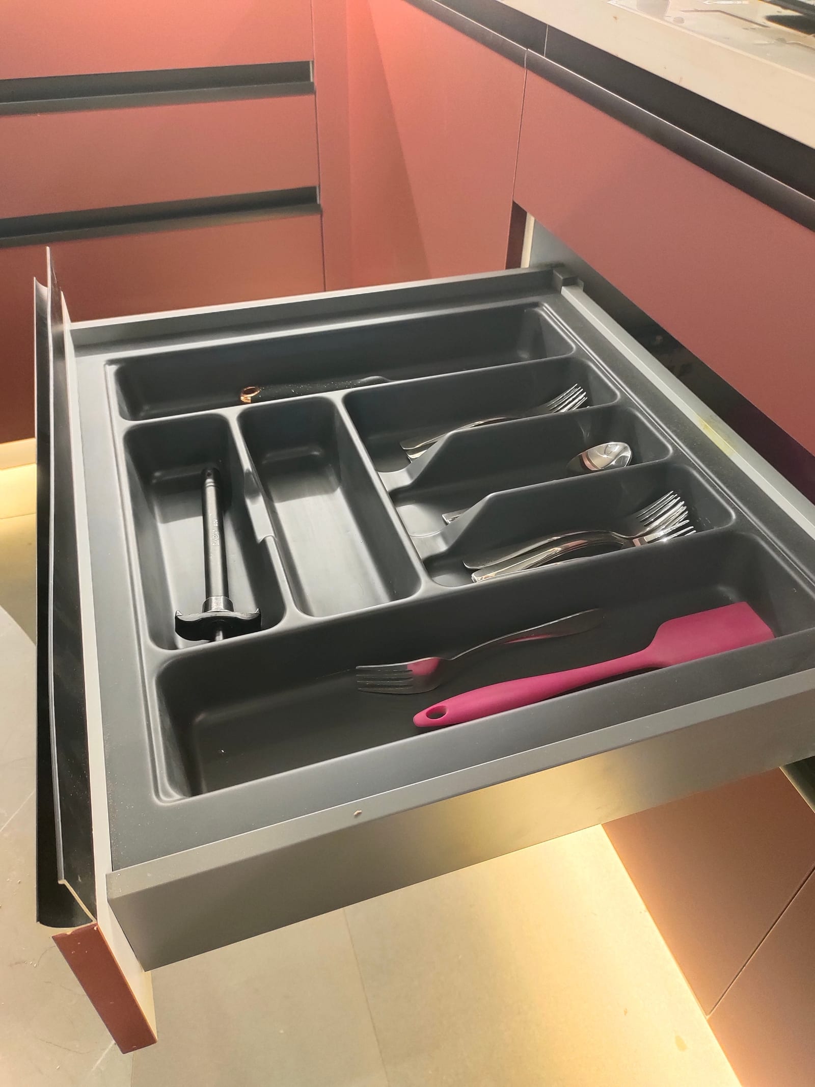 An open drawer fitted with a moulded dark grey cutlery tray divided into compartments