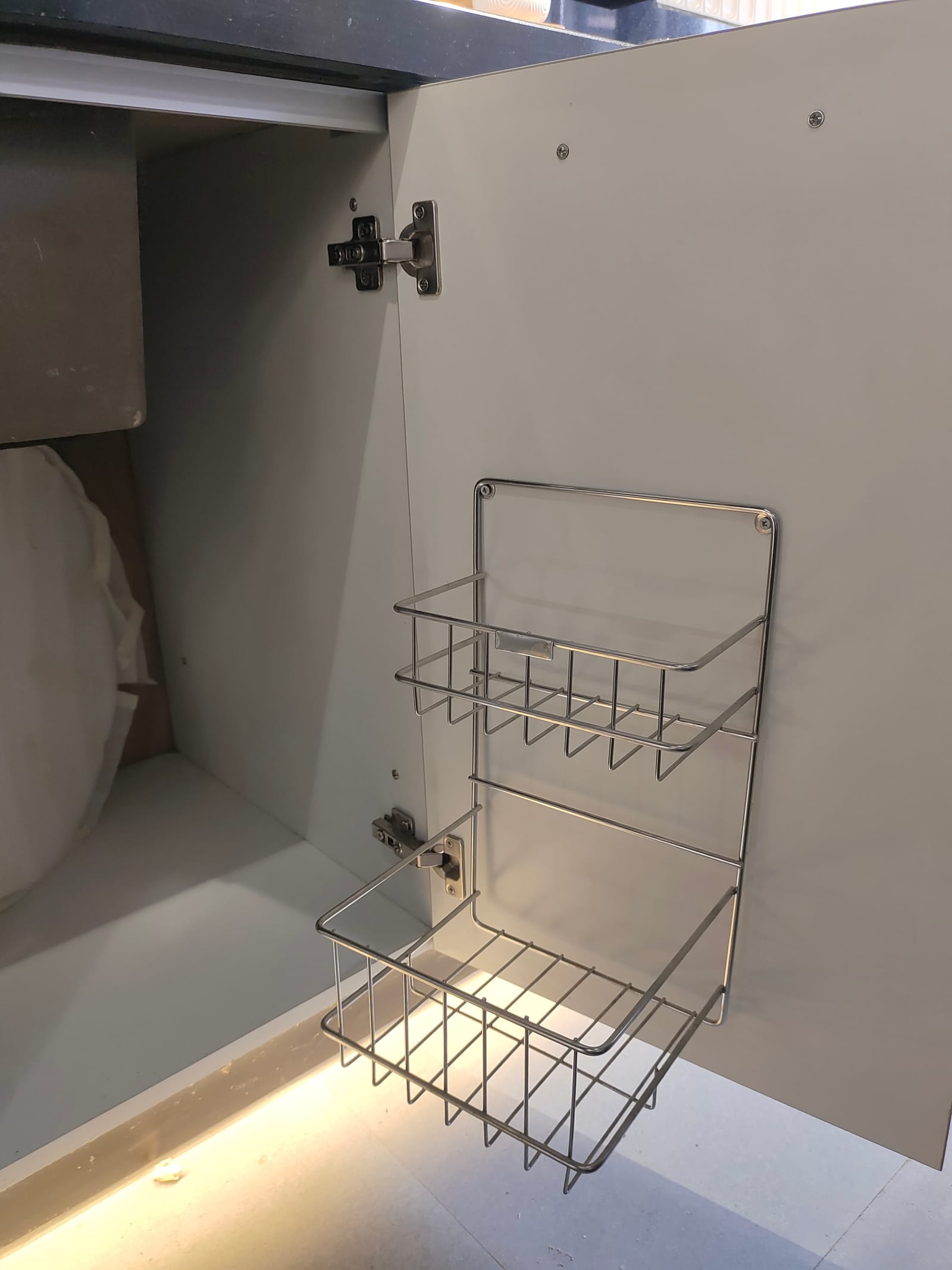 A two-tier wire basket fixed to the inside of a sink base unit door