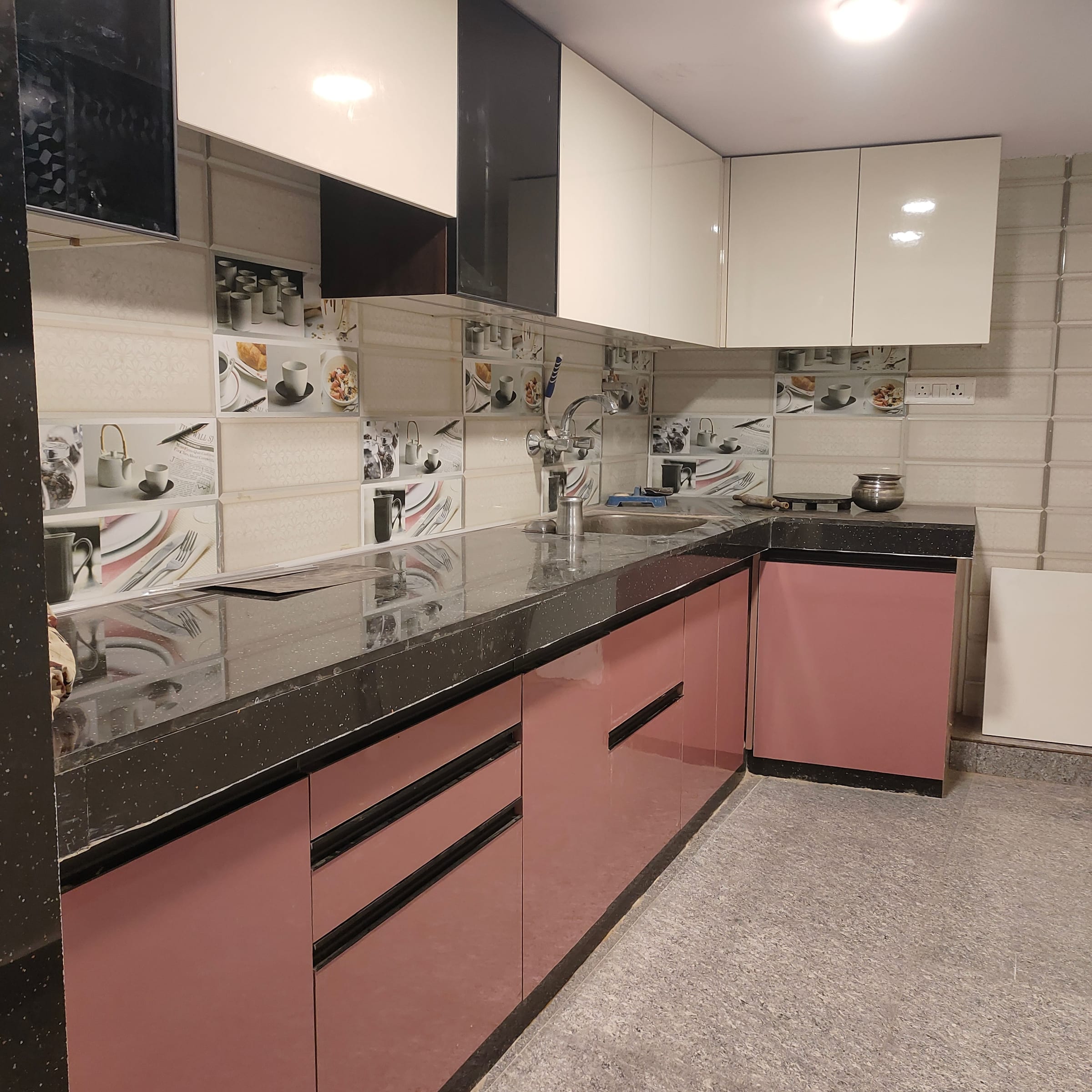 The corner of the finished kitchen from the same position, rose gloss base units and white and black wall cabinets meeting at the L