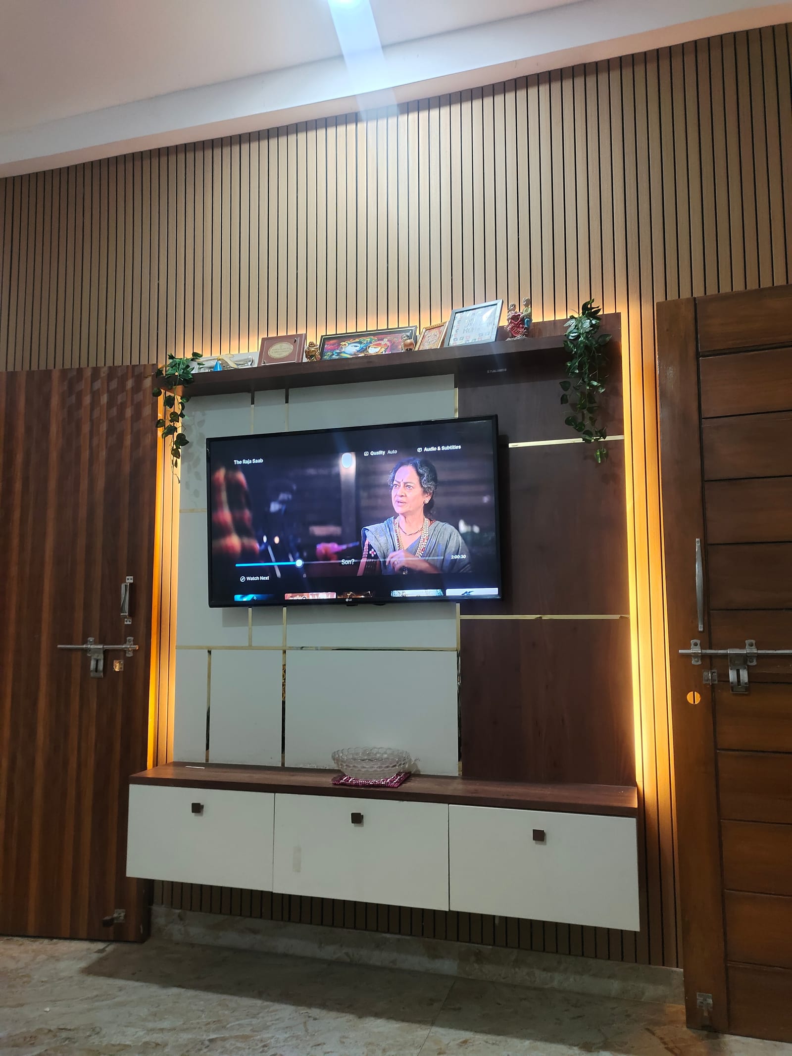 A television wall panelled floor to ceiling in fluted wood, with a walnut and white floating unit and cove lighting above