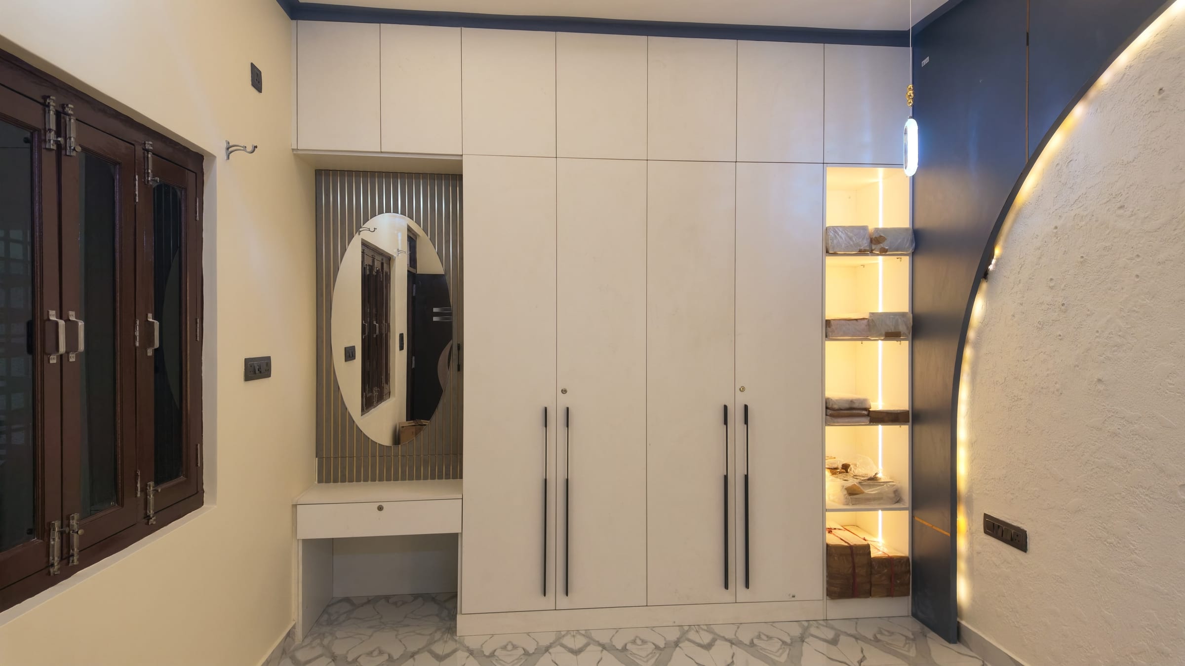A white six-door wardrobe run with a dressing table and oval mirror worked into one end and a lit display niche at the other